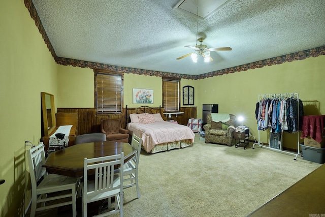 carpeted bedroom with a textured ceiling, wooden walls, and ceiling fan