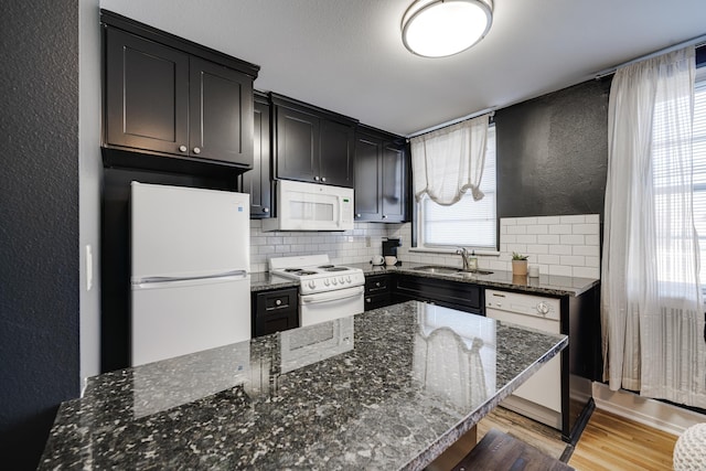 kitchen with dark stone counters, light wood-type flooring, backsplash, sink, and white appliances