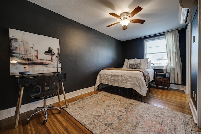 bedroom with hardwood / wood-style floors, a wall unit AC, and ceiling fan