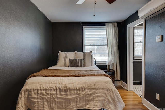 bedroom with wood-type flooring, ceiling fan, and a wall mounted air conditioner