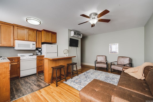 kitchen with a wall mounted AC, a breakfast bar area, dark wood-type flooring, white appliances, and ceiling fan