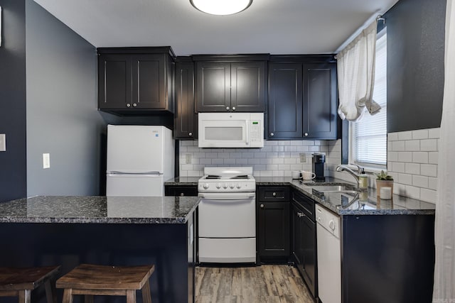 kitchen featuring light hardwood / wood-style flooring, dark stone counters, sink, and white appliances