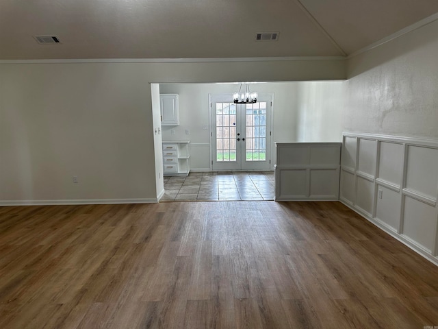 spare room featuring french doors, light hardwood / wood-style floors, ornamental molding, and a notable chandelier