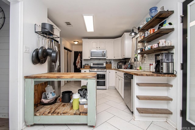 kitchen featuring sink, butcher block countertops, backsplash, white cabinetry, and appliances with stainless steel finishes