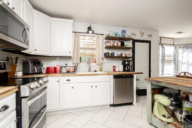 kitchen featuring butcher block counters, white cabinetry, appliances with stainless steel finishes, backsplash, and sink