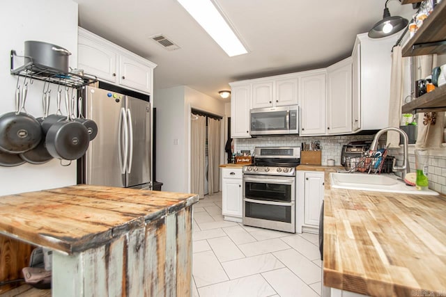 kitchen featuring butcher block counters, appliances with stainless steel finishes, decorative backsplash, and white cabinets