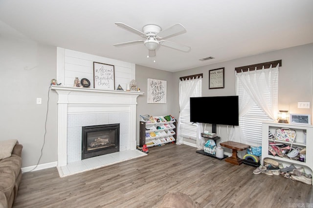 living room with ceiling fan, wood-type flooring, and a tiled fireplace