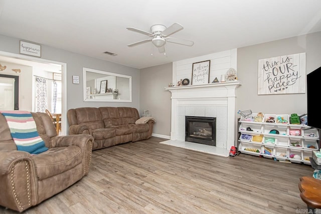 living room featuring a tiled fireplace, hardwood / wood-style floors, and ceiling fan