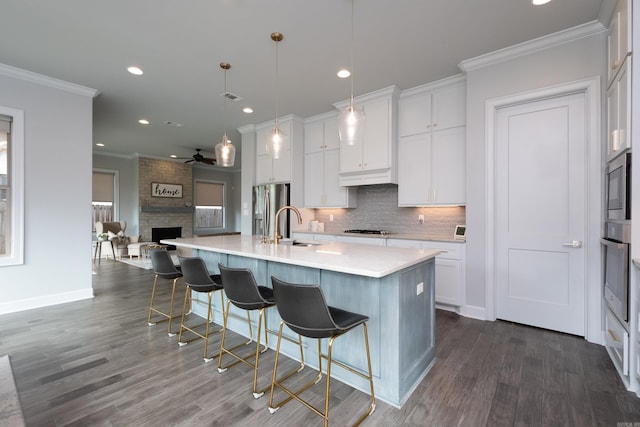 kitchen featuring dark wood-type flooring, pendant lighting, an island with sink, and white cabinets