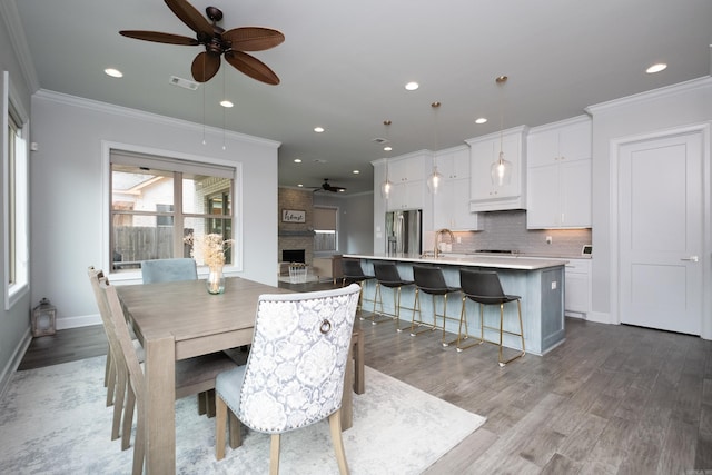 dining room with hardwood / wood-style floors, a fireplace, ceiling fan, and crown molding