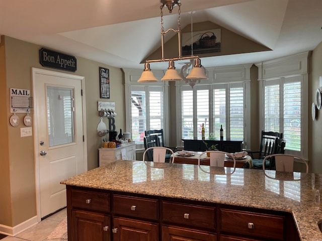 kitchen with light stone counters, vaulted ceiling, an inviting chandelier, light tile patterned flooring, and pendant lighting