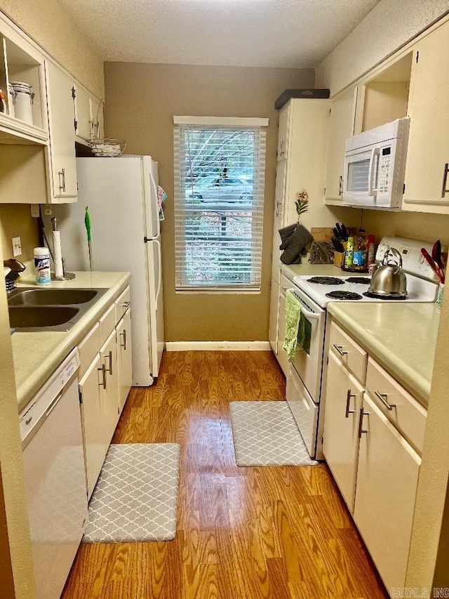 kitchen with white cabinetry, sink, white appliances, and light hardwood / wood-style floors