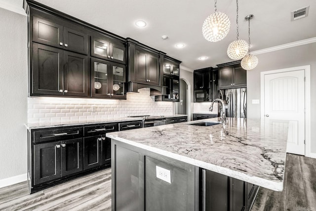 kitchen featuring ornamental molding, a large island with sink, sink, and decorative light fixtures