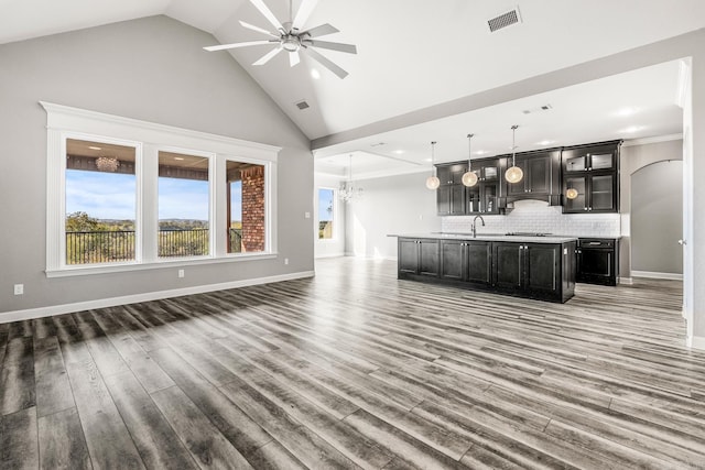 unfurnished living room featuring wood-type flooring, crown molding, high vaulted ceiling, sink, and ceiling fan with notable chandelier