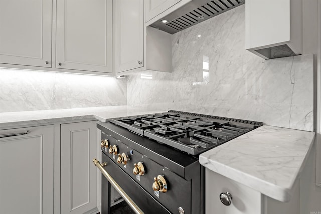 kitchen with custom range hood, high end range, light stone counters, and decorative backsplash