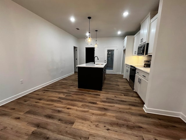 kitchen with white cabinets, dark wood-type flooring, appliances with stainless steel finishes, and a kitchen island with sink