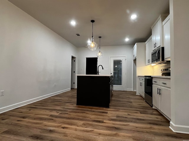 kitchen with stainless steel appliances, pendant lighting, white cabinets, dark wood-type flooring, and a kitchen island with sink