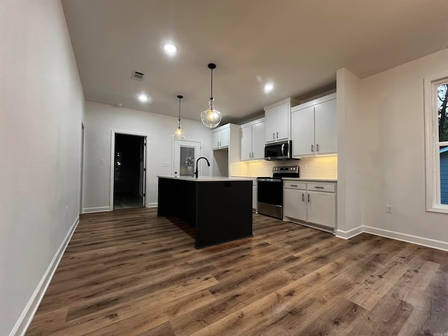 kitchen with white cabinetry, appliances with stainless steel finishes, decorative light fixtures, dark hardwood / wood-style floors, and a kitchen island with sink