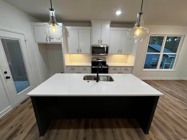 kitchen with white cabinets, appliances with stainless steel finishes, decorative light fixtures, and an island with sink