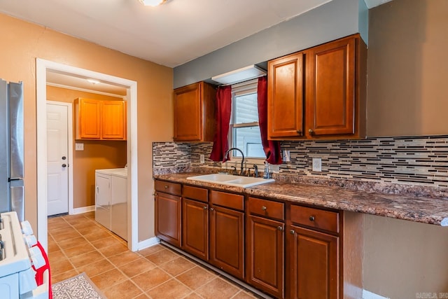 kitchen with sink, light tile patterned floors, backsplash, washer and clothes dryer, and stainless steel fridge