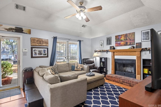 living room with wood-type flooring, vaulted ceiling, a textured ceiling, ceiling fan, and a fireplace