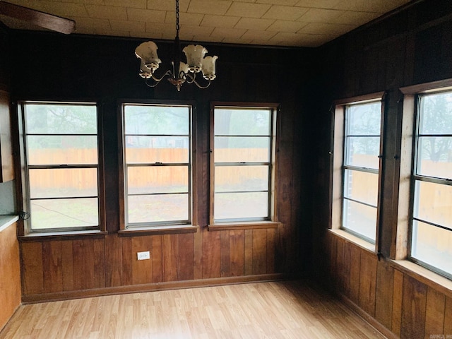 unfurnished dining area with wood walls, a chandelier, and light hardwood / wood-style flooring