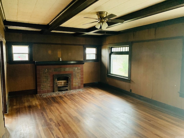 unfurnished living room with hardwood / wood-style flooring, beamed ceiling, ceiling fan, a fireplace, and wooden walls