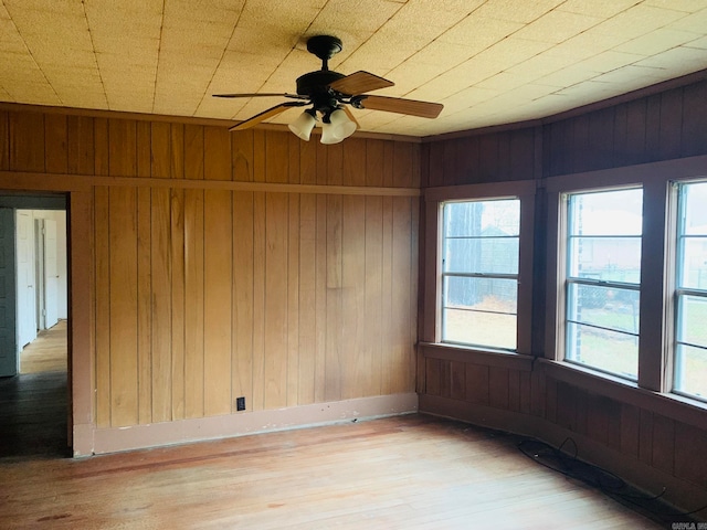 unfurnished room featuring wooden walls, ceiling fan, and light hardwood / wood-style flooring