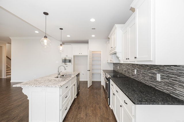 kitchen with sink, an island with sink, light stone countertops, white cabinetry, and appliances with stainless steel finishes