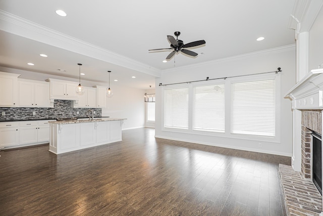 kitchen featuring a center island with sink, dark hardwood / wood-style floors, a fireplace, decorative light fixtures, and dark stone countertops