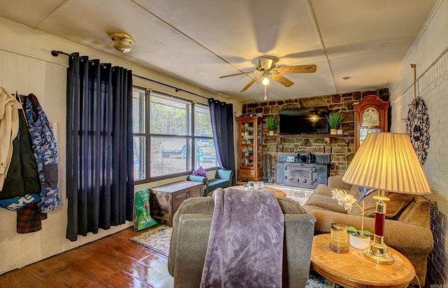 living room featuring a wood stove, hardwood / wood-style flooring, ceiling fan, and brick wall