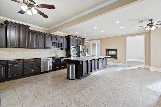 kitchen with dark brown cabinetry, tasteful backsplash, ornamental molding, a kitchen island, and appliances with stainless steel finishes