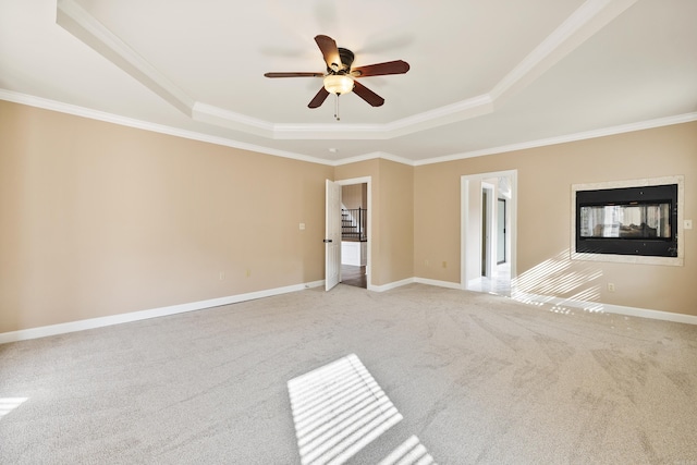 carpeted empty room featuring a multi sided fireplace, a raised ceiling, ceiling fan, and crown molding