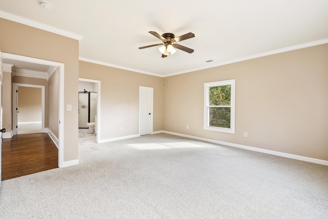 carpeted empty room featuring a barn door, ceiling fan, and crown molding