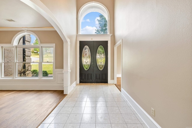 entrance foyer with ornamental molding, light wood-type flooring, a towering ceiling, and decorative columns