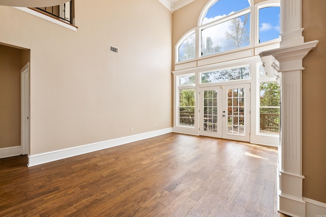 unfurnished living room with a wealth of natural light, wood-type flooring, french doors, and a towering ceiling