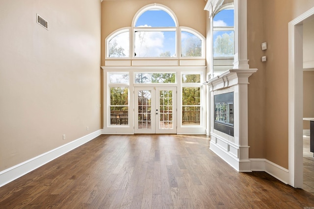 unfurnished living room with dark hardwood / wood-style flooring, french doors, and a towering ceiling