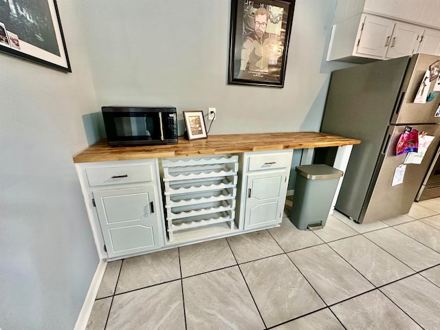 kitchen featuring white cabinets, butcher block counters, stainless steel fridge, and light tile patterned flooring