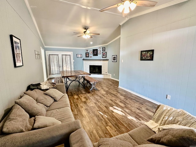 living room featuring wood-type flooring, ornamental molding, a fireplace, lofted ceiling, and ceiling fan