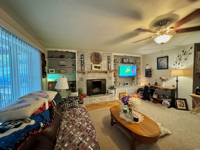 living room with built in shelves, carpet floors, a textured ceiling, ceiling fan, and a fireplace