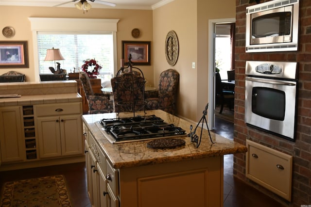 kitchen featuring cream cabinets, ceiling fan, crown molding, a kitchen island, and appliances with stainless steel finishes