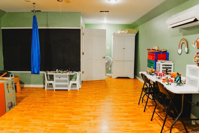 rec room with light wood-type flooring and a wall mounted air conditioner