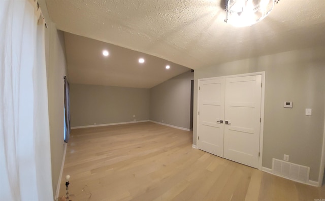 additional living space featuring lofted ceiling, a textured ceiling, and light hardwood / wood-style floors