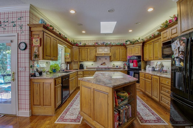 kitchen with black appliances, light stone countertops, crown molding, a center island, and light wood-type flooring