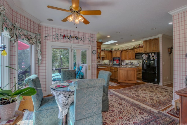 dining room with ceiling fan, a skylight, ornamental molding, and light wood-type flooring