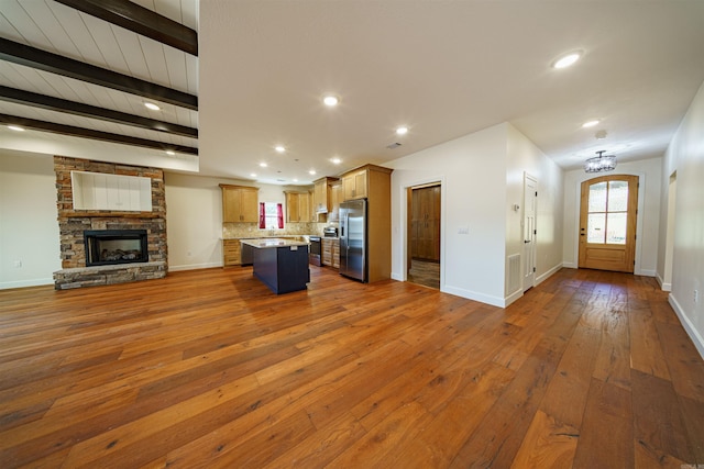 kitchen featuring a stone fireplace, dark wood-type flooring, a center island, a breakfast bar area, and stainless steel fridge with ice dispenser