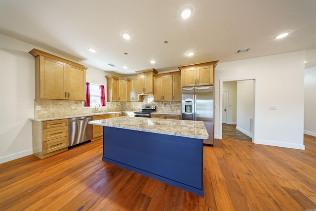 kitchen with dark hardwood / wood-style flooring, light stone countertops, a kitchen island, and appliances with stainless steel finishes