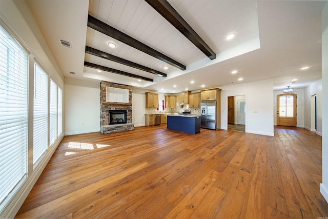 unfurnished living room with light hardwood / wood-style floors, a stone fireplace, and beam ceiling