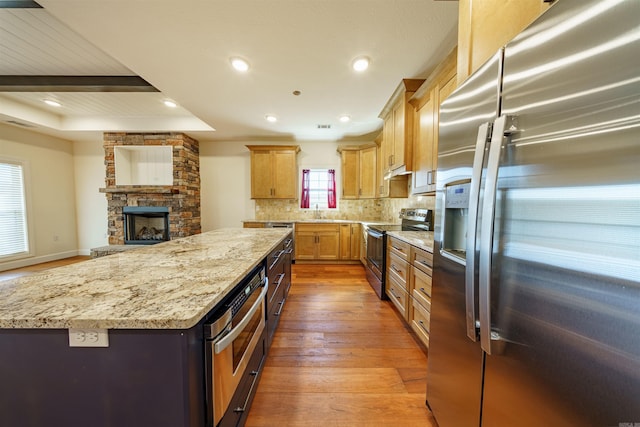 kitchen featuring stainless steel appliances, light stone counters, a center island, hardwood / wood-style flooring, and a fireplace