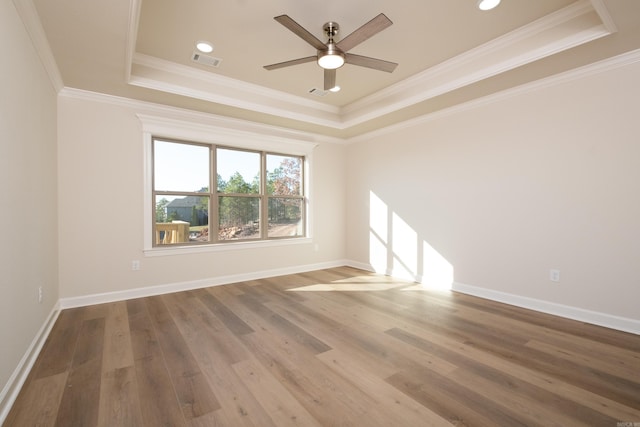 empty room with a raised ceiling, crown molding, and hardwood / wood-style floors